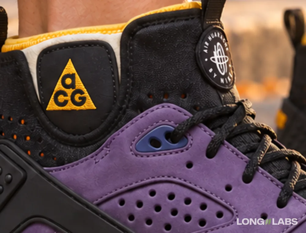 Generated close-up of the sneaker's ankle collar: a yellow triangle logo with clean letters on a black patch, a round black badge with white text, the purple side panel with its holes below.